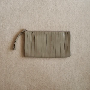 Beige kuvertväska med fransar - Stilren beige kuvertväska med fransdetaljer och dragkedja upptill. 