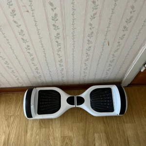 Vit hoverboard från Deaver  - Säljer en vit hoverboard från Denver med svarta detaljer och gummiplattor för fötterna. Hoverboarden har rundade former och är tillverkad i plast med gummihjul. Perfekt för att ta sig fram snabbt och smidigt.dene lite slitet
