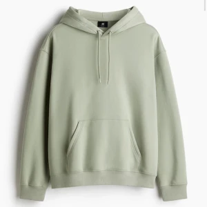 Ljusgrön hoodie från H&M - Snygg ljusgrön hoodie från H&M med huva och dragsko. Tröjan har en klassisk känguruficka framtill och ribbade muddar vid ärmslut och nederkant. Perfekt för en avslappnad stil.