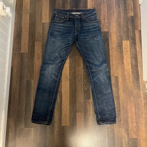  Steady Eddie Nudie Jeans - Säljer ett par mörkblå jeans från Nudie Jeans, modell Steady Eddie. Klassisk femficksdesign med orangea sömmar och regular passform. Tillverkade i 100% ekologisk bomull. Perfekta för dig som gillar en tidlös jeansstil.