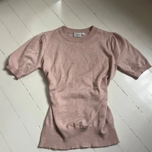 Ljusrosa stickad topp - Säljer en ljusrosa stickad topp. Modellen har korta puffärmar, rund halsringning och ribbade kanter vid ärmslut och nederkant. Perfekt för en söt och stilren look. Knappt använd. Skriv för fler bilder.