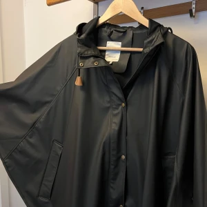 Svart regnjacka från Soyaconcept - Säljer en svart regnjacka från Soyaconcept i storlek XS. Jackan har huva, tryckknappar och dragkedja framtill samt fickor på sidorna. Perfekt för regniga dagar och enkel att matcha med olika outfits.