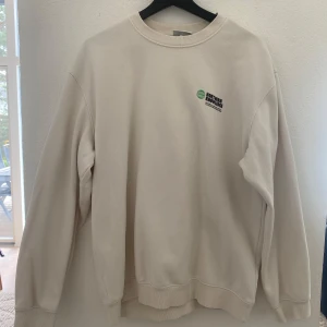 Beige sweatshirt från H&M med tryck - Säljer en beige sweatshirt från H&M med trycket 'Northern Knowledge' och en grön glob på bröstet samt stort tryck på ryggen. Tröjan har relaxed fit, rund hals och långa ärmar. Perfekt för en chill och stilren look.