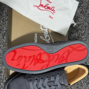 Gråa sneakers från Christian Louboutin - Säljer ett par gråa sneakers från Christian Louboutin med klassisk röd sula och snörning. Skorna har en stilren design i mocka och kommer med originalkartong och dustbag. Perfekta för dig som vill sticka ut med exklusiva detaljer.
