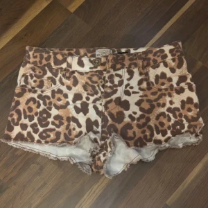 Leopardmönstrade shorts River Island - Snygga leopardmönstrade shorts från River Island med råa kanter och klassisk femficksdesign. Shortsen är i jeansmaterial och har knappar och bälteshällor. Perfekta för dig som vill sticka ut med ett djurmönster.