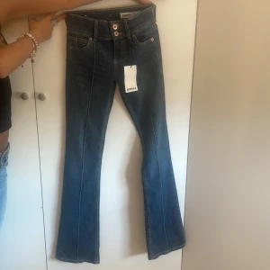 Blå bootcut jeans från Bershka - Snygga blå jeans från Bershka i bootcut-modell med klassisk femficksdesign och markerade sömmar framtill. Jeansen har normal passform och stängs med två knappar och dragkedja. Perfekta för dig som gillar en retrovibe och vill ha ett par jeans som sticker ut. Säljer dom då dom är för långa 