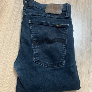 Nudie Jeans - Snygga svarta jeans från Nudie Jeans med klassisk femficksdesign och coola broderade detaljer på bakfickorna. Modellen har smal passform och är tillverkad i mjukt jeanstyg med stretch. Perfekt för dig som gillar stilrena och moderna jeans. Knappt använda, inköpta för runt 1,5 mitt priss 899kr. Hör av er vid frågor👑