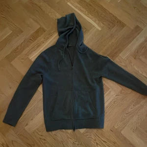 Mörkgrå Kashmir hoodie från Singular society, M - Mörkgrå hoodie från Singular society i stickat kashmir material. Tröjan har dragkedja framtill, huva med snörning och två fickor. Perfekt för dig som gillar en clean och enkel stil med lite oversized känsla. Passar till chill dagar och när du vill vara bekväm. De en kashmir hoodie