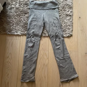 Grå stickade byxor från Gina Tricot - Grå stickade yoga pants från Gina Tricot med bred ribbad midja. Byxorna har en rak passform med lätt utsvängda ben och är perfekta för chill dagar. Supermjukt material som känns skönt mot huden.