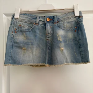 Blå jeanskjol med slitningar - Snygg kort jeanskjol i ljusblå tvätt från Bershka Denim med slitna detaljer och fransad kant nedtill. Då dragkedjan gått sönder har jag nu gjort en egen lösning så den funkar som vanligt, därav pris.