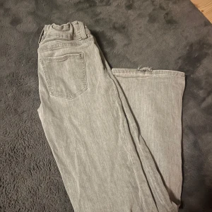 Lågmidjade jeans från Gina  - Säljer ett par grå jeans, lågmidjade med klassisk femficksdesign. Jeansen har dubbla knappar i midjan och en snygg, lite tvättad look. Perfekta för dig som gillar en enkel och stilren vibe.