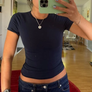 Mörkblå tight t-shirt - Säljer en mörkblå, tight t-shirt med korta ärmar och rund hals. T-shirten är croppad och sitter snyggt figurnära. Perfekt till jeans eller kjol och har en enkel, stilren look utan mönster eller detaljer. Materialet känns mjukt och stretchigt.