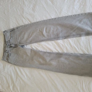Grå raka jeans i vintage-look - Snygga grå jeans med rak passform och klassisk femficksdesign. Jeansen har en ljusgrå tvätt och raka ben, perfekt för en avslappnad stil. Tillverkade i bomull och har detaljer som nitar och bälteshällor.