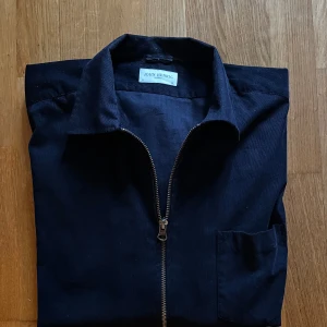 Overshirt från John Henric - Snygg mörkblå overshirt från John Henric med klassisk krage och grov dragkedja framtill. Tillverkad i mjuk manchester som ger en cool och lite retro känsla. Perfekt att slänga över en t-shirt för en avslappnad look. Storlek 43 som passar L-XL. Hör av dig vid funderingar! Priset är inte hugget i sten👍 Mvh Carl 