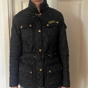 Svart quiltad jacka från Barbour - Quiltad svart jacka från Barbour  med bälte i midjan använt 2 gånger i helt nyskick! Så så fin till våren