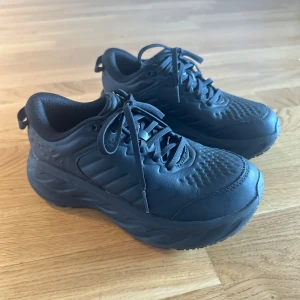 Hoka Bondi SR Wide - Helt nya oanvända Hoka Bondi SR Wide för kvinnor med bredare fötter. Storlek 38  Bondi SR är den mest dämpade skon i HOKAs sortiment. Vattenavvisande läder, en halkfri yttersula och EVA-mellansula för att garantera dämpning hela dagen, har denna arbetsplatskrigare ett ultragreppigt, heltäckande gummi som klarar kraven från både servicebranschen och sjukvården. Perfekt för hösten när det blir kyligare och ofta blöt.  BÄST FÖR: Landsvägslöpning Komfort