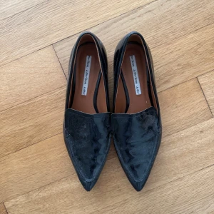 Svarta lackloafers med spetsig tå - Snygga svarta loafers från & Other Stories i glansigt lackmaterial. Skorna har en spetsig tå och låg klack, vilket ger en stilren och modern look. Perfekta för dig som gillar att sticka ut med klassiska detaljer och vill ha något som funkar till många outfits.