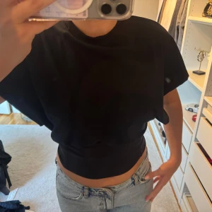Svart croppad t-shirt - Svart croppad t-shirt med korta ärmar och rund hals. T-shirten har en loose passform upptill och sitter tightare vid midjan. (Endast spegeln som är smutsig)