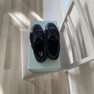 Svarta sneakers från Lanvin i mocka - Snygga svarta sneakers från Lanvin med ovandel i mocka och lackad tå. Skorna har vita gummisulor och svarta skosnören. Klassisk låg modell som passar perfekt till jeans eller dressat. Kommer med originalkartong.