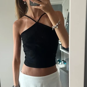 Svart ribbad croppad linnetopp - Säljer en svart croppad topp med smala axelband som korsas framtill. Toppen är ribbad och har en tight passform som framhäver figuren. Perfekt för att styla med kjol eller jeans för en trendig look. Från Ginatricot. Passar både S och M.