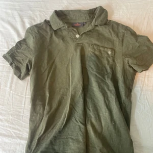 Olivgrön piké från Morris, storlek S - Snygg olivgrön pikétröja från Morris med klassisk krage, korta ärmar och bröstficka med broderad logga. Tillverkad i mjuk bomull som känns skön mot huden. Perfekt för en avslappnad men stilren look. Pris kan diskuteras. 