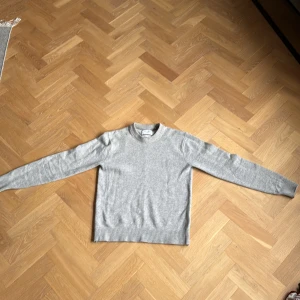 Ljusgrå stickad tröja i ullblandning - En stilren ljusgrå stickad tröja från Vailent i mjuk ullblandning. Tröjan har rund halsringning, ribbade muddar och lång ärm. Perfekt för lager-på-lager och enkel att matcha med jeans. Tröjan är använd ett fåtal gånger och är i mycket bra skick.