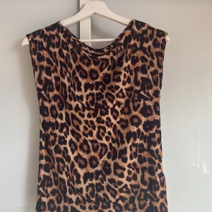 Leopardmönstrad ärmlös topp 157 S - Säljer en ärmlös topp från 157 i storlek S med ett riktigt snyggt leopardmönster. Toppen har en lös passform och är perfekt för dig som vill sticka ut med djurmönster. Färgerna går i brunt, svart och beige och materialet känns lätt och skönt mot huden.