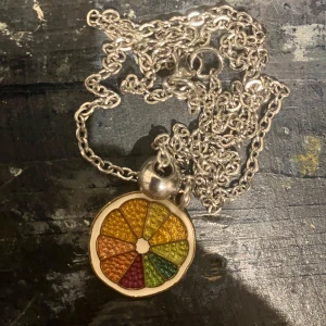 Färgglatt citrus halsband  - Unikt halsband med en rund berlock som ser ut som en citrusfrukt i flera färger: orange, gul, grön och röd. Kedjan är i silverfärgad metall och berlocken har en cool textur. Perfekt för dig som gillar färg och vill sticka ut.