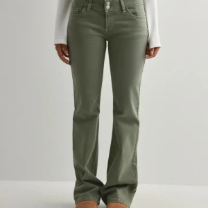 Olivgröna bootcut jeans med broderi - Snygga olivgröna jeans med bootcut passform och hög midja. Byxorna har dubbla knappar framtill, klassiska fickor och coolt broderi på bakfickorna. Perfekta för dig som vill ha en trendig och bekväm look med lite edge.