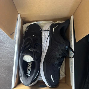 Hoka W Clifton 10, 38 2/3 - Hoka Women Clifton 10 i svart/vitt. Nästintill oanvända, var i fel storlek och returnerades inte i tid. Storlek 38 2/3 EU, nypris 1999kr💗