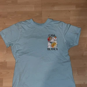 Ljusblå t-shirt från Casablanca - Snygg ljusblå t-shirt från Casablanca Tennis Club med coolt konstnärligt tryck på både bröstet och ryggen. T-shirten har klassisk passform och är gjord i mjuk bomull. Perfekt för dig som gillar unika prints och streetwear-vibe.