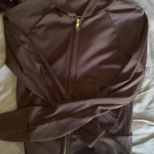 Svart hoodie med dragkedja - Snygg brun hoodie med dragkedja framtill och huva. Tröjan har långa ärmar, ribbade muddar och en stor ficka på magen. Perfekt för chill dagar eller när du vill ha en enkel och stilren look.