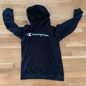 Svart Champion hoodie - Svart hoodie från Champion i storlek XL med broderad logga på bröstet. Klassisk känguruficka framtill och huva. Perfekt för dig som gillar streetwear och vill ha en enkel men snygg tröja med tydlig branding.
