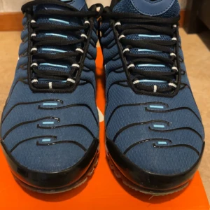 Nike Air Max Plus blå sneakers - Nike Air Max Plus sneakers i blått med svarta och vita detaljer. Storlek 45 men passar även 44 .Snyggt vågmönster på ovansidan, svart snörning och vit sula med synliga Air-enheter. Tn Air-logga på hälen och meshmaterial för skön ventilation. Perfekt för dig som gillar streetwear och sportig stil.