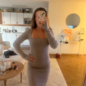 Beige ribbad långärmad klänning - Säljer en beige ribbad klänning med lång ärm och fyrkantig ringning. Klänningen är figurnära och har en mjuk stickad känsla som sitter snyggt på kroppen. 