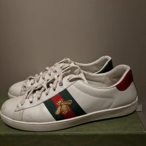Gucci skor - Äkta Gucci Ace sneakers i vitt skinn med klassiska gröna och röda ränder på sidan, broderad guldfärgad bi och metallicröd samt metallicgrön häl. Skorna har snörning och rund tå, och kommer med originalkartong och dustbags.