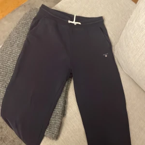 Svarta mjukisbyxor från Gant - Svarta mjukisbyxor från Gant med vit snörning i midjan och diskret logga på ena benet. Byxorna har en avslappnad passform och är perfekta för chill dagar. Mjukt material och fickor på sidorna.