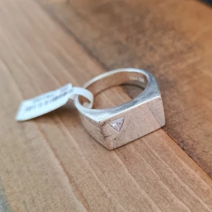 Sterling klackring med triangelformad sten - Stilren och chunky ring i äkta silver (925) med en infattad liten, klar triangel-slipad sten på framsidan. Ringen har en fyrkantig, modern form som ger ett coolt och edgy intryck. Ringen är 20mm och är helt ny med tag. Därför inte helt putsad (för att inte förstöra etiketten).
