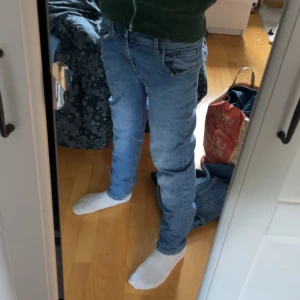 Blå jeans från Jack & Jones - Säljer ett par klassiska blå jeans från Jack & Jones med normal passform och raka ben. Jeansen har fem fickor, snygga kontrastsömmar och knappstängning framtill. Perfekt för dig som gillar enkel och stilren denim med lite faded effekt.