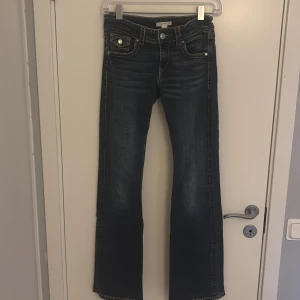 Mörkblå bootcut jeans Gina Tricot - Snygga mörkblå bootcut jeans från Gina Tricot med kontrastsömmar och coola fickdetaljer med knappar både fram och bak. Jeansen har klassisk femficksdesign och är tillverkade i jeansmaterial med lätt tvättad look.
