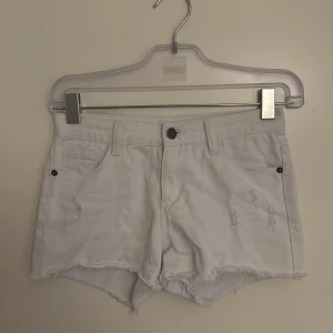 Vita low waist minishorts  - Snygga vita jeansshorts från UNIQ dnm med fransig kant och slitna detaljer framtill. Klassisk femficksmodell med knapp och dragkedja. Perfekta för varma dagar och en chill look.