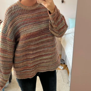 Randig stickad tröja i höstiga färger - Mysig stickad tröja med breda ränder i brunt, beige, rost, grått och inslag av grönt. Tröjan har en loose passform, rund halsringning och långa ärmar. Perfekt för lager på lager och chill dagar.