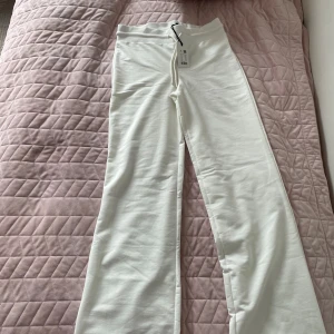 Vita vida mjukisbyxor med snörning - Säljer ett par fräscha vita mjukisbyxor med vida ben och snörning i midjan. Byxorna har hög midja och är gjorda i mjukt bomullsmaterial, perfekta för en chill och avslappnad stil.