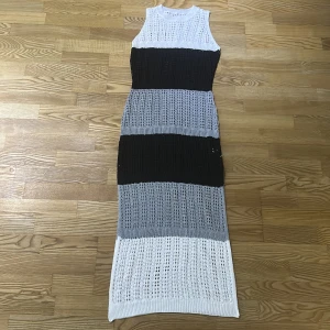 Stickad långklänning i svart, grått och vitt - Snygg stickad långklänning med breda blockränder i svart, grått och vitt. Ärmlös modell med rund hals och genombruten stickning som ger en luftig känsla. Perfekt för dig som gillar en chill och trendig look.