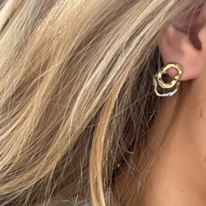 Chunky örhängen i guld och silver - Säljer ett par chunky örhängen med cool organisk form i både guld och silver. De har en unik, vågig design med två sammanlänkade ringar i metall. Perfekt för dig som gillar statement-smycken och vill sticka ut med en modern vibe.