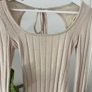 Beige ribbad topp med öppen rygg - Supersnygg beige ribbad topp med långa ärmar och öppen rygg som knyts i nacken. Helt oanvänd, storlek S, från Nelly😍💞