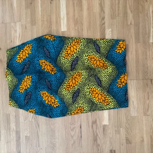 Färgglad blommig långkjol - Säljer en unik långkjol med blommigt mönster i starka färger. Kjolen har orange och gula blommor mot blå och svarta detaljer, med inslag av grönt. Materialet känns som bomull och kjolen har en rak form. Perfekt för dig som gillar färg och mönster!