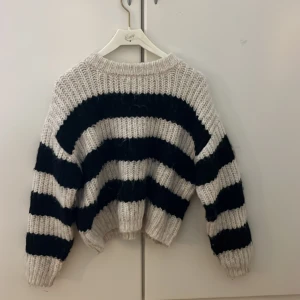 Randig stickad tröja från Zara - Säljer en chunky stickad tröja från Zara i storlek 152. Tröjan har breda svarta och vita ränder, rund hals och långärmade. Den är loose fit och har en mysig, grovstickad känsla som är perfekt för kyliga dagar.