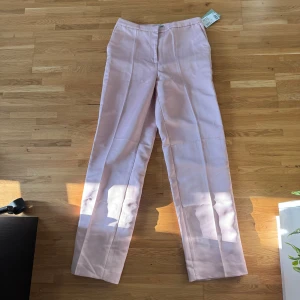 Ljusrosa kostymbyxor från H&M - Snygga ljusrosa kostymbyxor från H&M i storlek 38. Byxorna har raka ben, pressveck och en klassisk midja. Materialet är mjuk polyester som ger en skön och stilren känsla. Perfekt för dig som vill ha en clean och fräsch look.