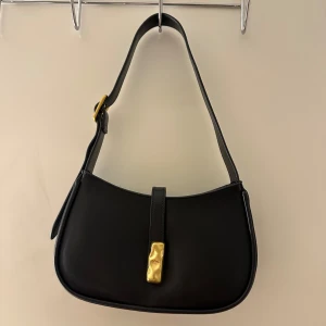 Svart axelväska med gulddspänne - Handväska från GinaTricot. Aldrig använd